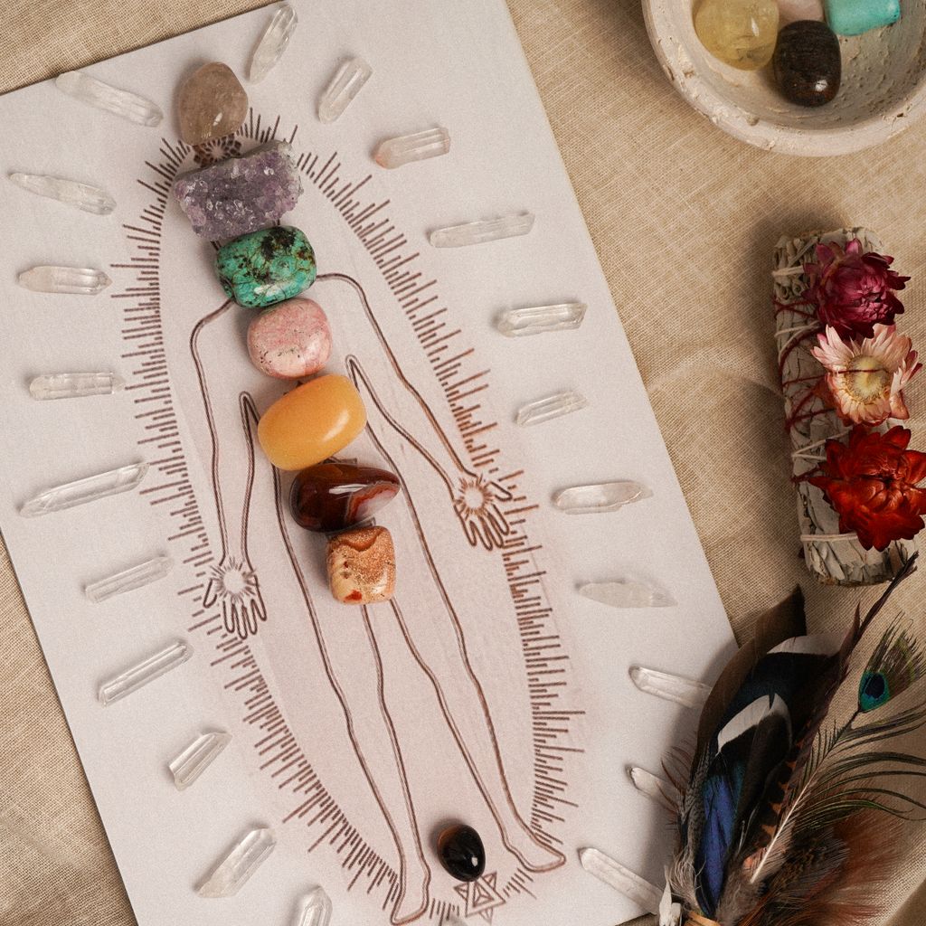 Arrangement of healing crystals on a chakra body illustration with sage and feathers.
